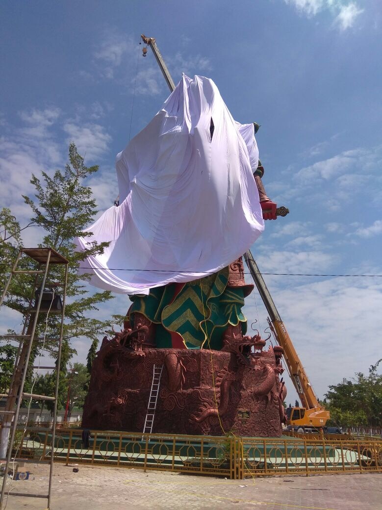 A crane is used to cover the statue with a large sheet.