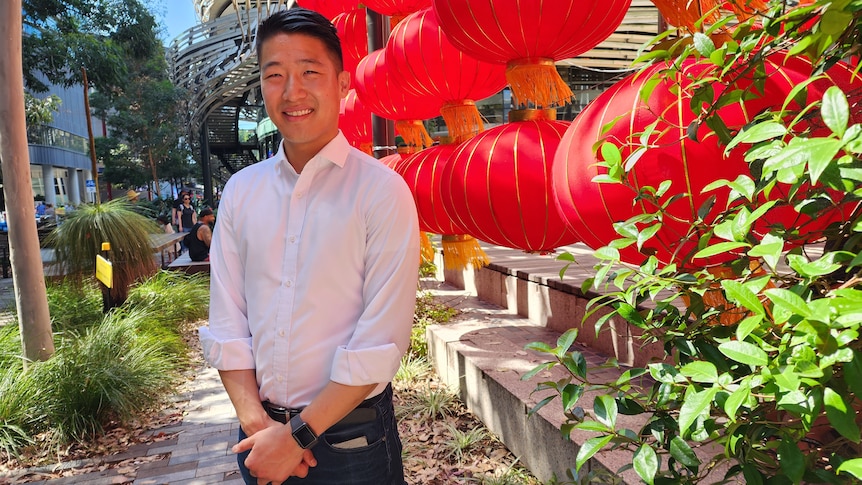 a young man smiling with his hands crossed standing on front of chinese paper lanterns