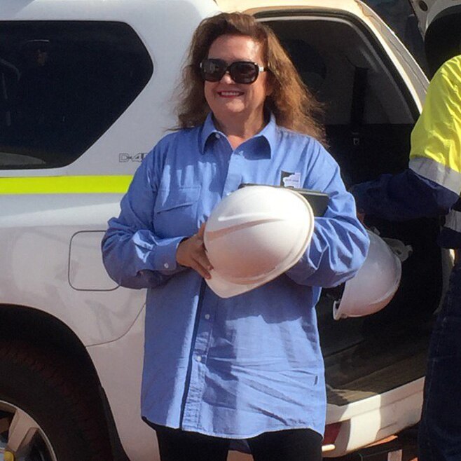 Gina Rinehart stands next to a car smiling and holding a hard hat.