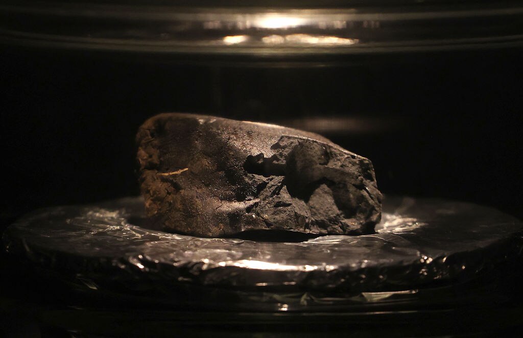 A large black meteorite is seen in a museum display case