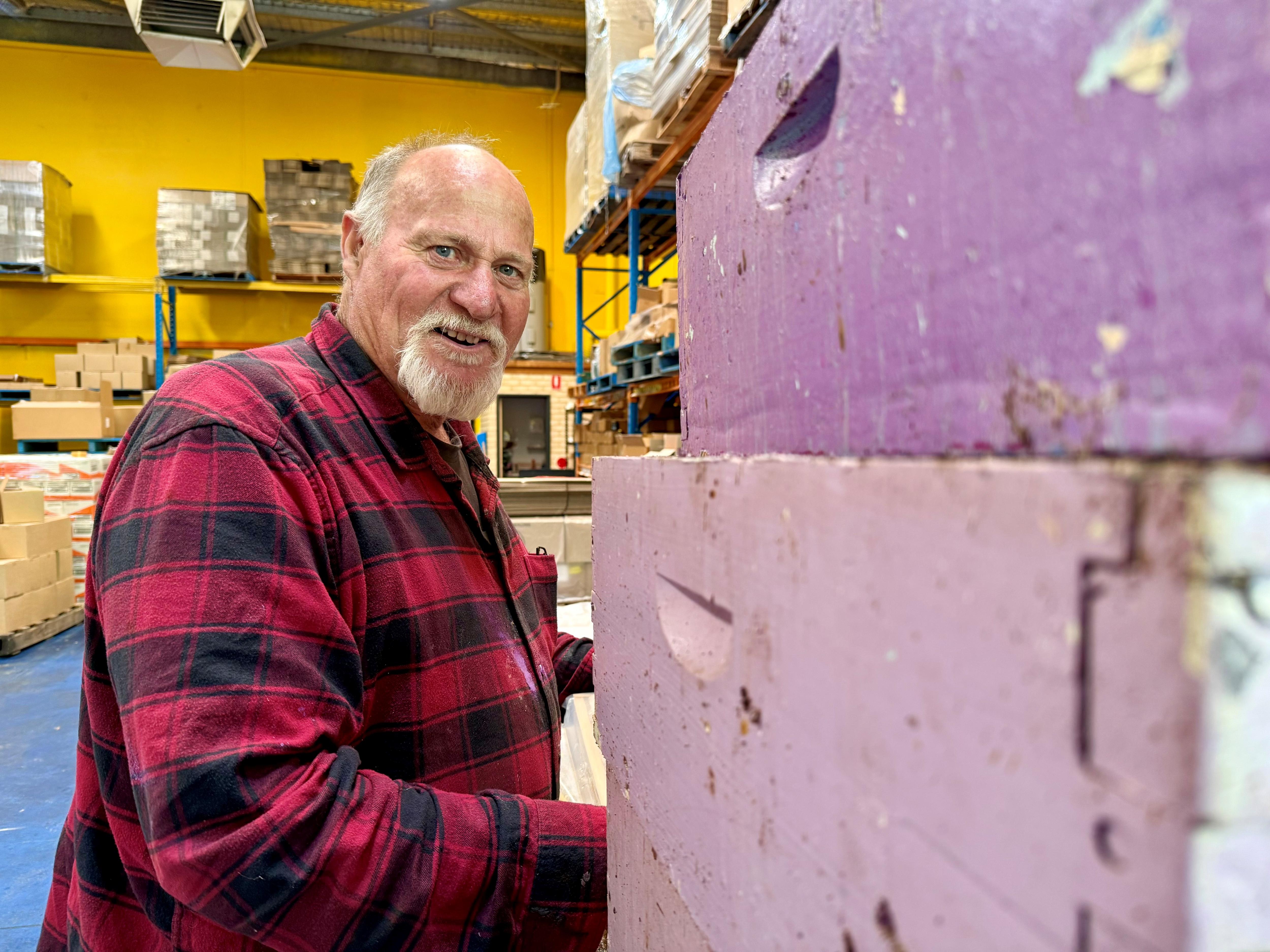 Un hombre se inclina cerca de coloridas colmenas.