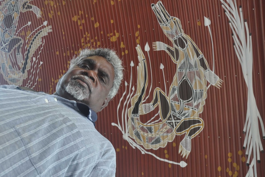 Aboriginal leader Yingiya Guyula with a mural of crocodiles behind him.