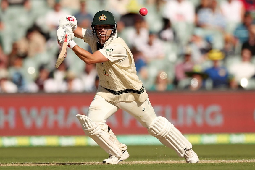 An Australian batsman plays on the offside, as the ball flies through the air during a Test match.