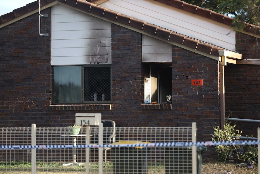 A low-set brick house with fire damage in the windows.