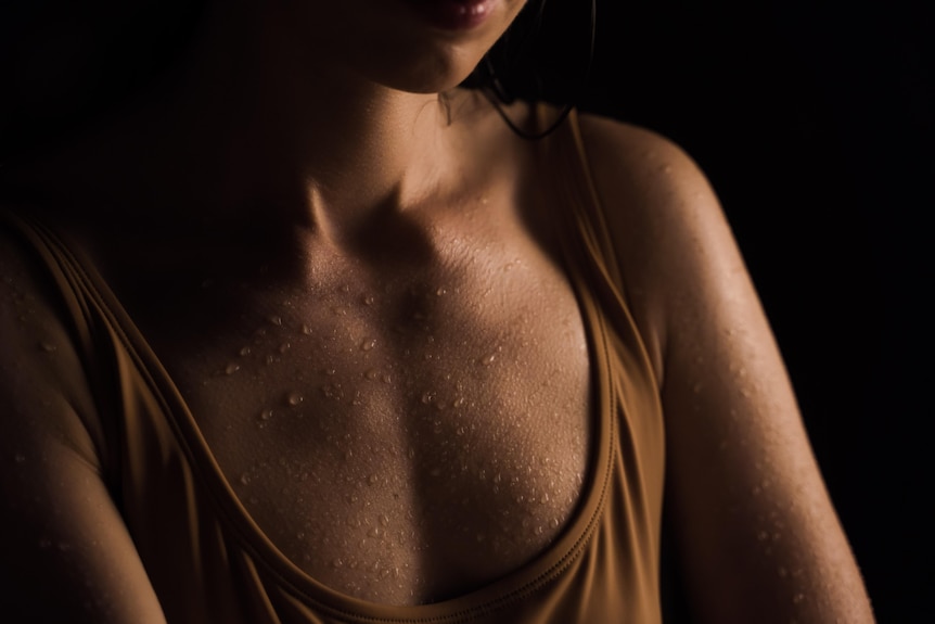 A woman in a tan coloured singlet with beads of sweat across her chest