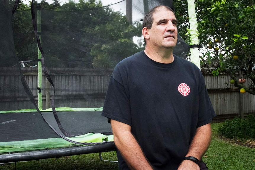 Mr Mantaris in a black t-shirt stands in front of a netted trampoline/.