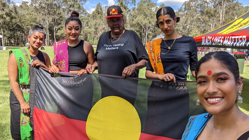 South Asian Australian Women dressed in traditional Indian clothing standing an Aboriginal woman holding the Aboriginal flag