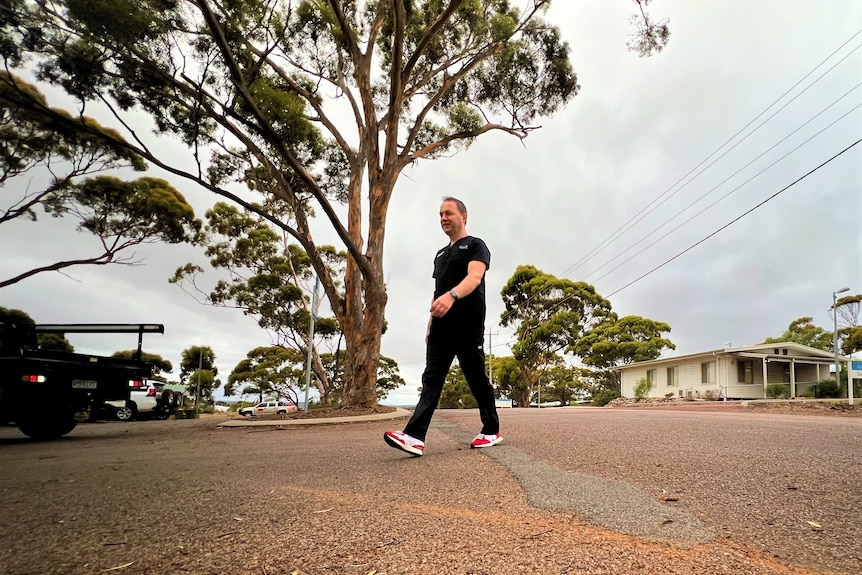 He walks past a tall gum tree and wears red sneakers, photo taken from low