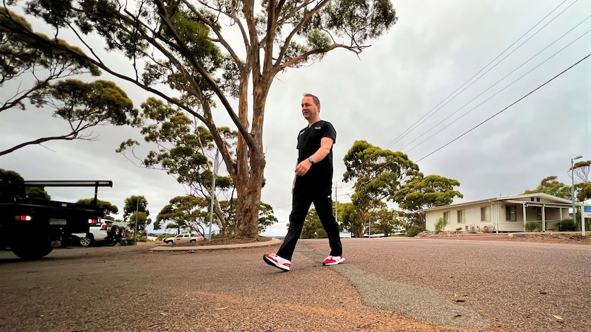 He walks past a tall gum tree and wears red sneakers, photo taken from low
