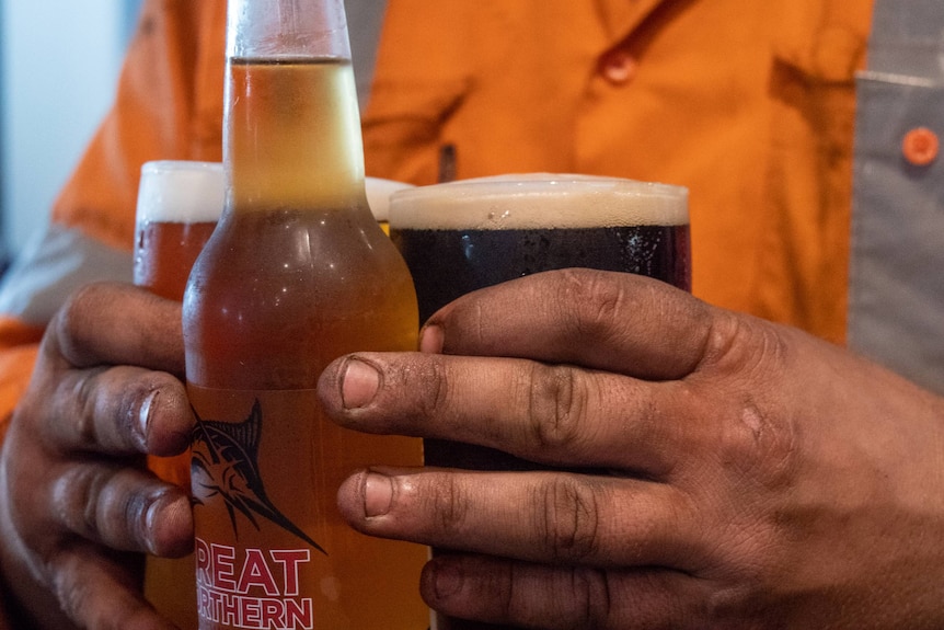 close up of a tradie with coal stained hands carrying a few beers