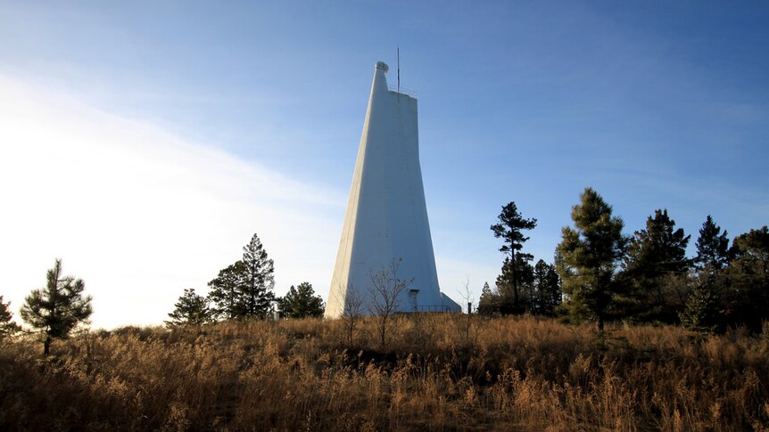Sunset over the Dunn Solar Telescope in Sunspot, New Mexico. It is a big white pyramid-shaped tower in a wooded area.