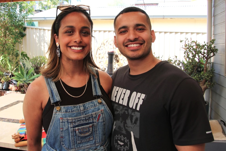 a couple, a man and a woman, smile at the camera while hugging and standing outdoors at a sydney suburb