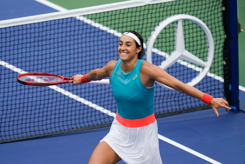 A tennis player holds her arms out to the side while grinning madly after her win at the US Open.