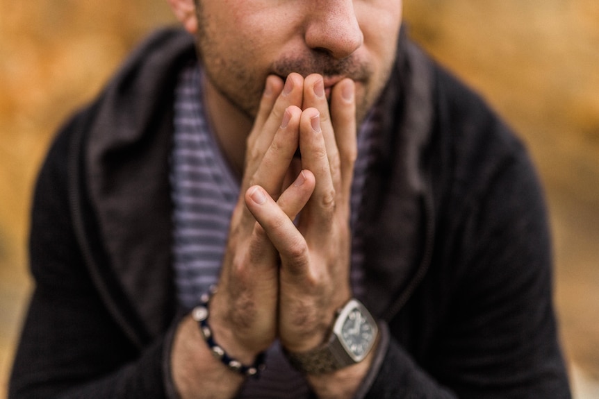 A close up of a man's hands placed together in front of his body in a worried pose.