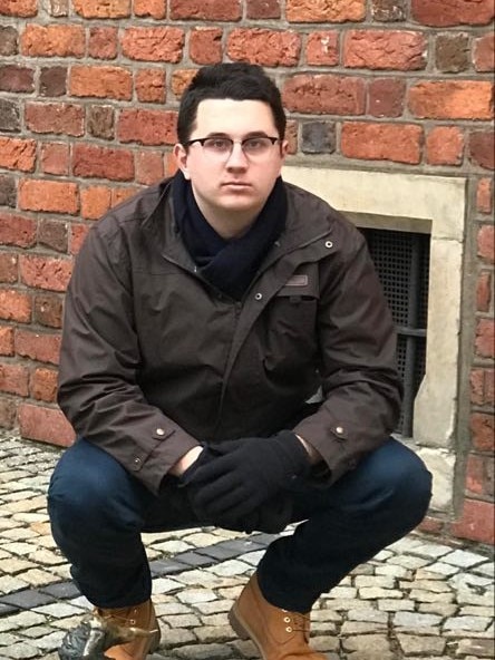 A young man posing in front of a brick wall.