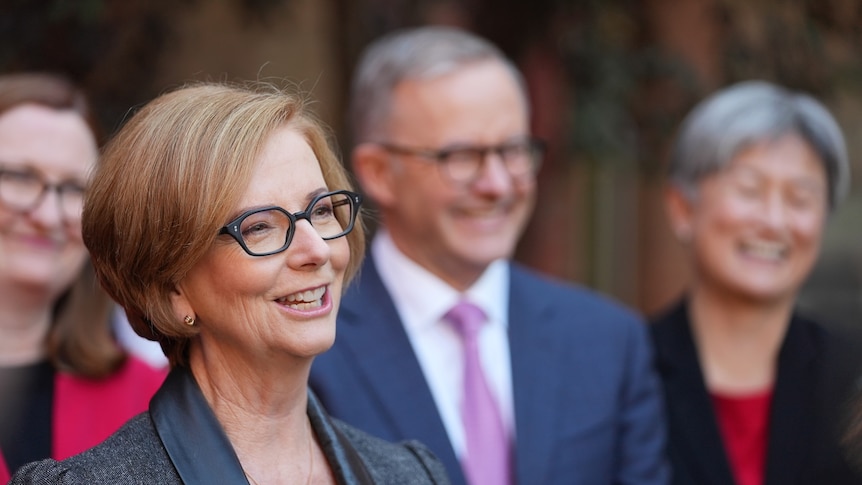 Julia Gillard smiles while standing in front of anthony albanese and penny wong