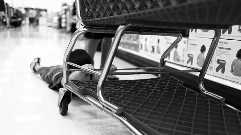 A child is lying on the ground and holding on desperately to a shopping trolley