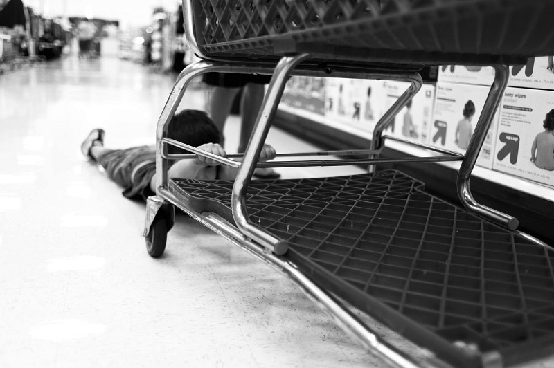 A child is lying on the ground and holding on desperately to a shopping trolley