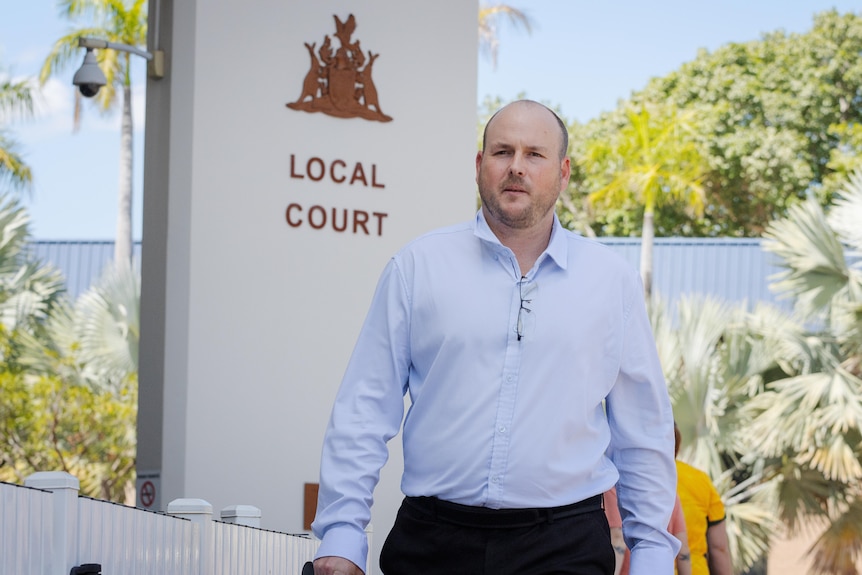 A man in a light blue dress shirt walks away from the Darwin Local Court