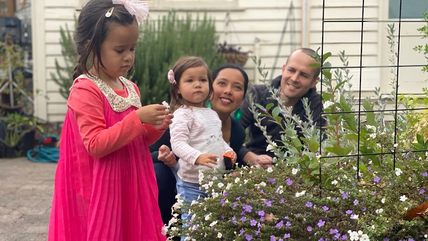 A man and woman with two little girls squat near a bed of flowers.