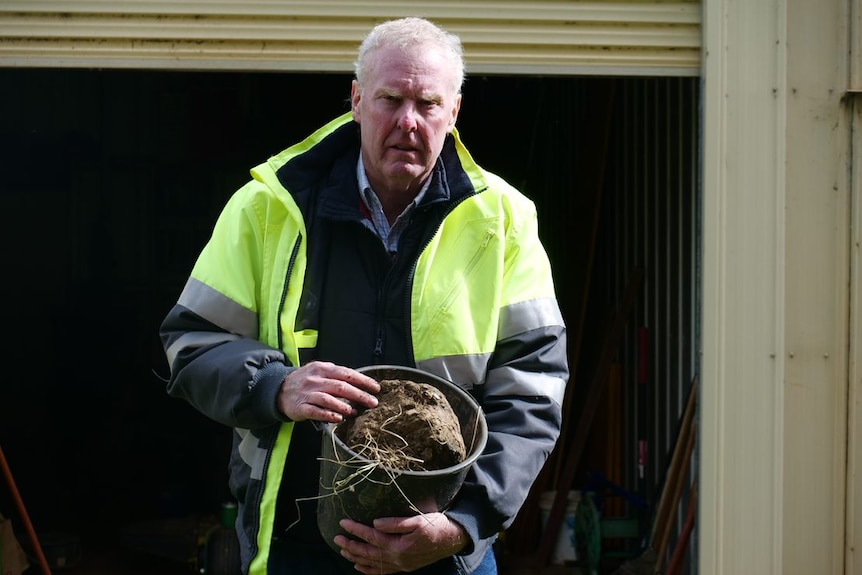 A middle-aged man in a high-vis parka, holding a bucket full of mud.