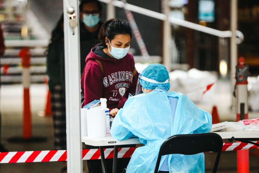 a lady wearing a mask approaches a healthcare worker also wearing a mask