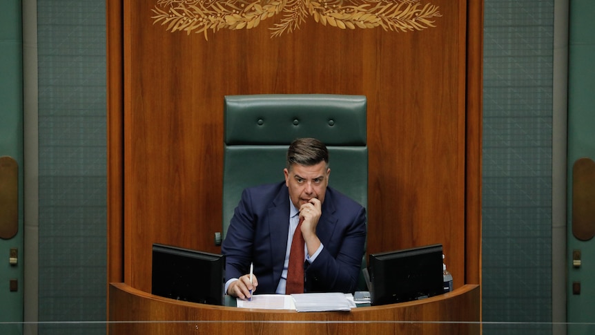 Milton Dick sitsin the speakers chair with his left hand to his mouth, looking to the right