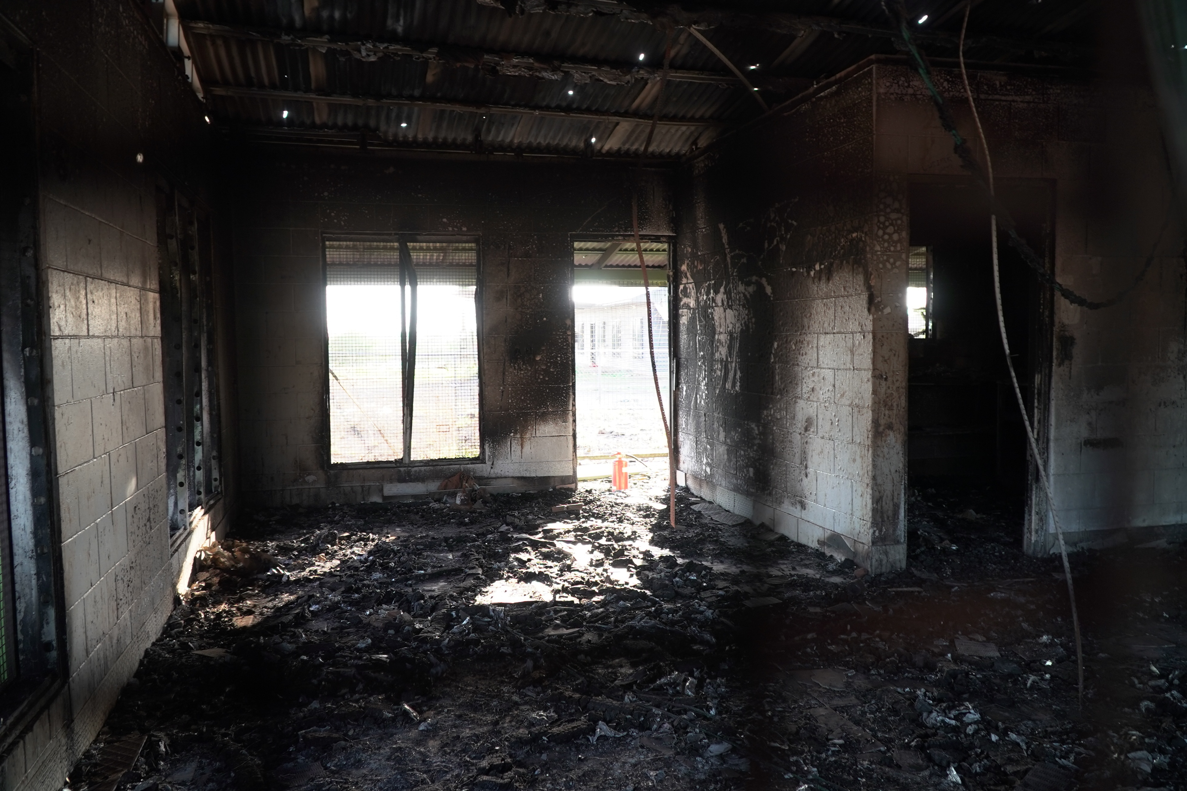 The interior of an empty, burned out house with the floor covered in a thick layer of ash and charcoal.