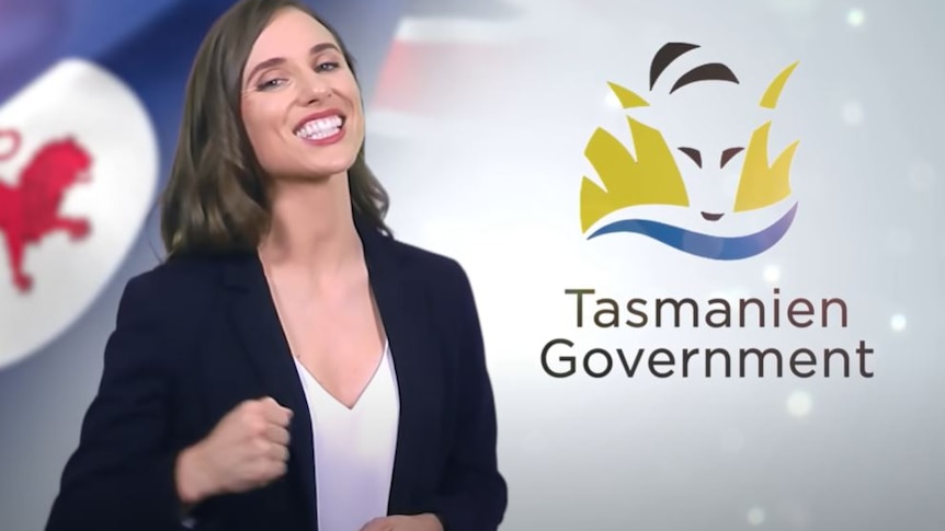 A woman in a black blazer smiles at the camera in front of a fake 'Tasmanien government' background