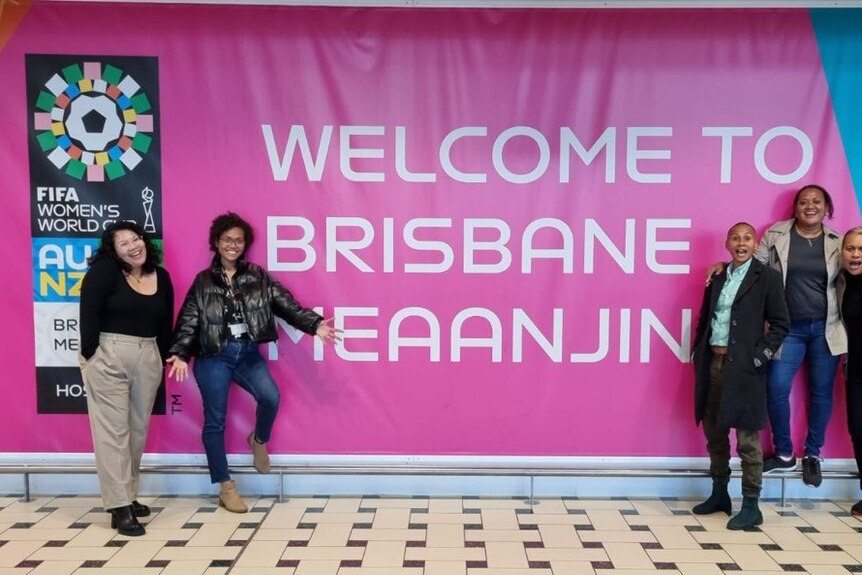 Women standing in front of Birsbane airport sign 