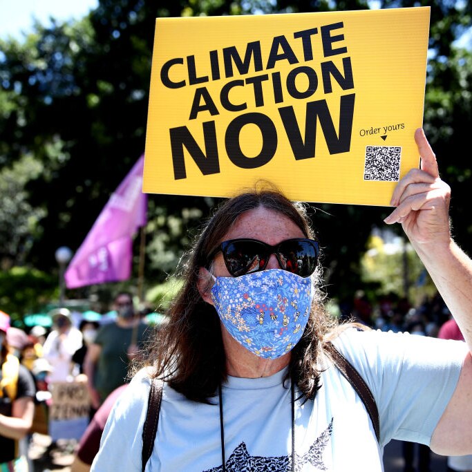 A woman protester holds up a sign saying 'climate action now'