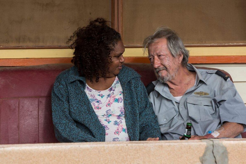 Ningali Lawford-Wolf and Michael Caton look at each other on a couch in a still from the film Last Cab to Darwin.
