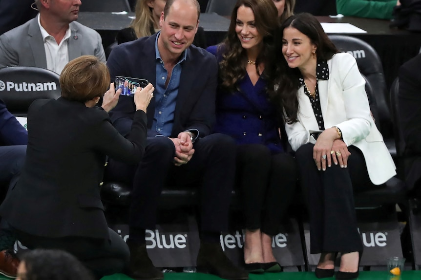 Prince William and Princess Kate sit to pose for a photo with a woman wearing a white blazer.