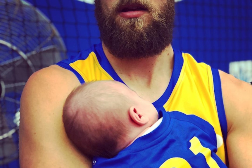 A bearded West Coast Eagles player holds a baby wearing a Number 31 guernsey.