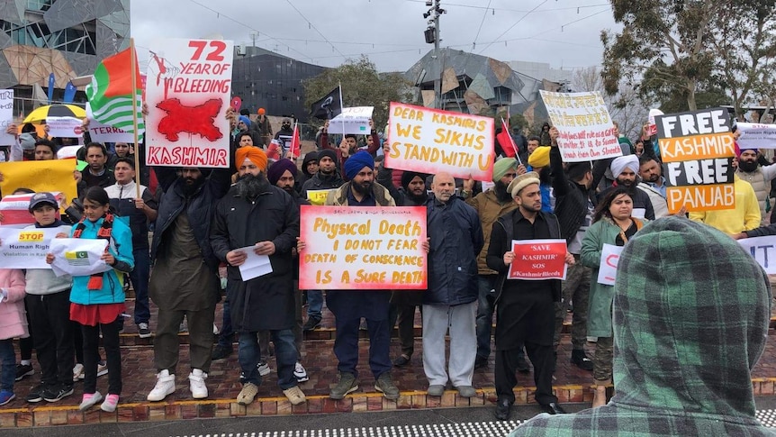Люди стоят на Фед-сквер в Мельбурне с табличками с надписью «72 года кровотечения в Кашмире. Мы, сикхи, мы поддерживаем вас».