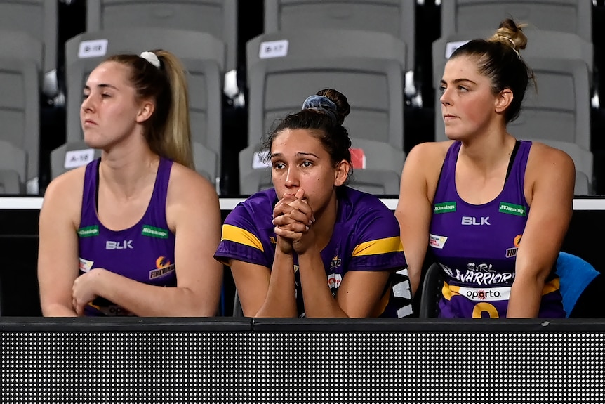 Three netballers leaning on the bench during a match 