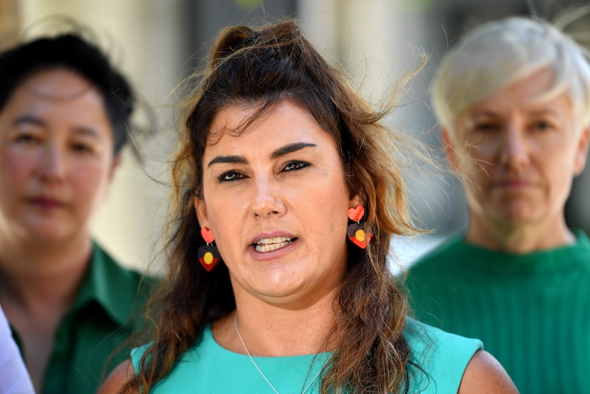 Lidia speaks at a press conference whikle wearing Indigenous flag earring.