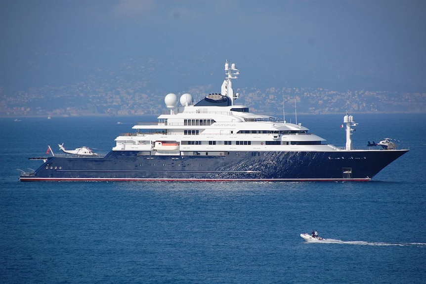 A small motor boat heads towards large, multi-storey luxury yacht carrying two helicopters