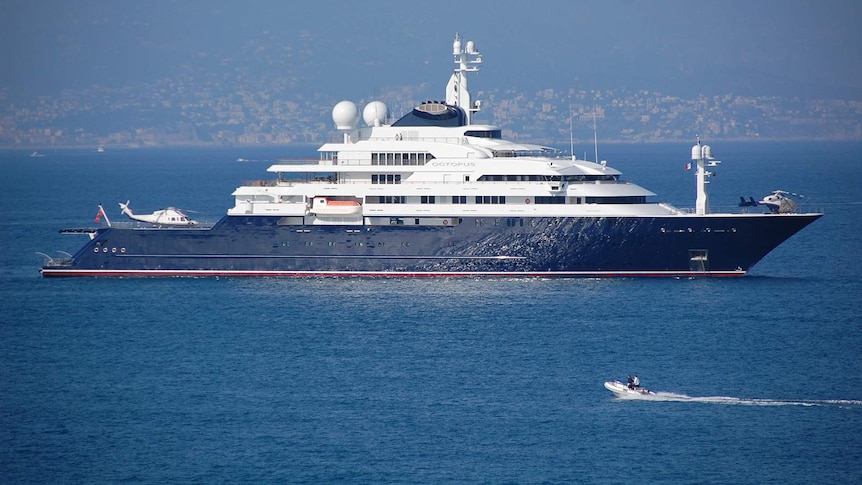 A small motor boat heads towards large, multi-storey luxury yacht carrying two helicopters