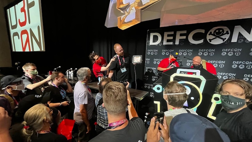 a wide shot with a crowd in the foerground filming a man holding a tablet device on stage