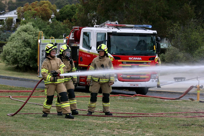 Three women firefighters train with a hose in front of a fire truck