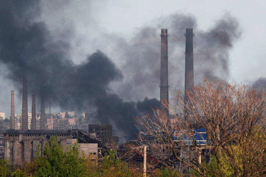 Smoke rises above a steel plant during a war.