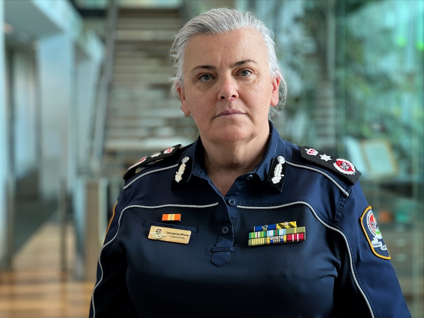 A woman with grey hair in an emergency services uniform looks serious.