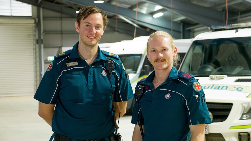 two male paramedics in uniform standing in an ambulance depot