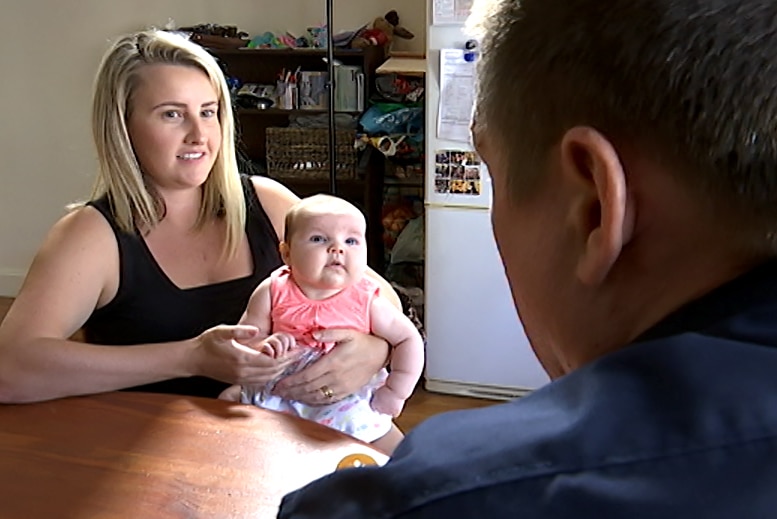 A woman holding a three-month-old baby talking to a man who is facing away from the camera.