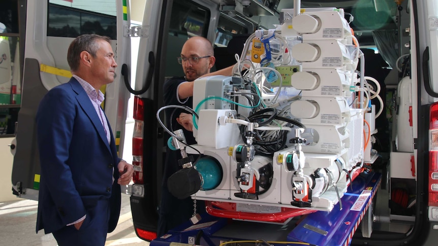 Health Minister Roger Cook is shown a neonatal transport cot at the back of an ambulance outside Princess Margaret Hospital.
