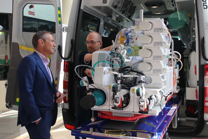 Health Minister Roger Cook is shown a neonatal transport cot at the back of an ambulance outside Princess Margaret Hospital.