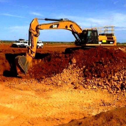 A large excavator is digging a hole from red dirt at a gold mine.
