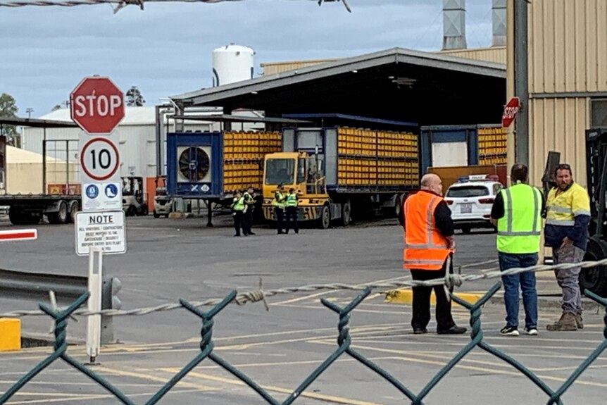 Police and other people in high-vis vests stand in front of a yellow semi-trailer