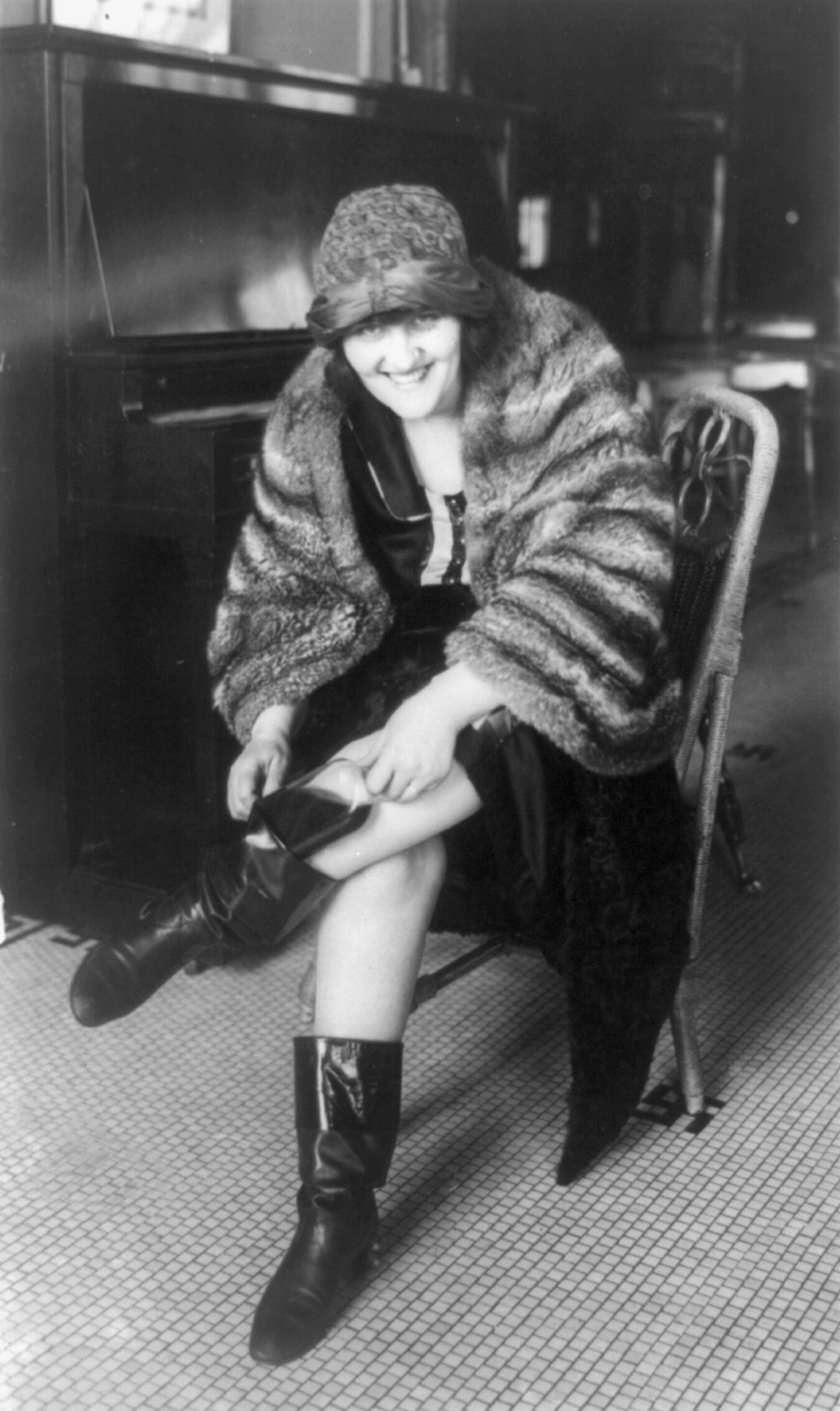 A black and white photo of a 1920s woman putting a flask in her boot.